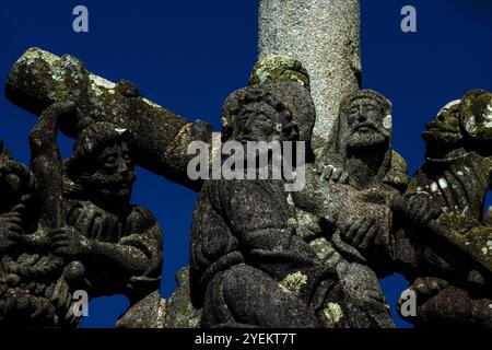 Christ porte une lourde croix à sa crucifixion. Détail de la procession Road to Golgotha, sculpté fin des années 1500 sur la face sud du calvaire dans la paroisse proche de l'Eglise Saint-Miliau à Guimiliau, Finistère, Bretagne, France. Immédiatement derrière le Christ, un soldat vêtu d'un uniforme militaire contemporain tire sur la croix et la pèse. La route du Golgotha / Calvaire ou via Dolorosa est le nom donné au dernier voyage du Christ de Jérusalem à la colline du Golgotha, où il a été crucifié. Banque D'Images