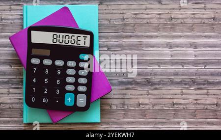 Le mot budget sur l'écran de la calculatrice, sur une table en bois avec des cahiers Banque D'Images