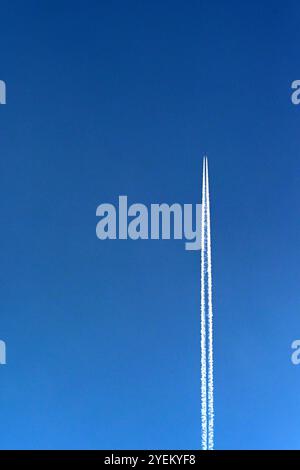 L'avion des vacances traîne des traînées blanches à travers un ciel bleu profond. Concept de voyage. Banque D'Images