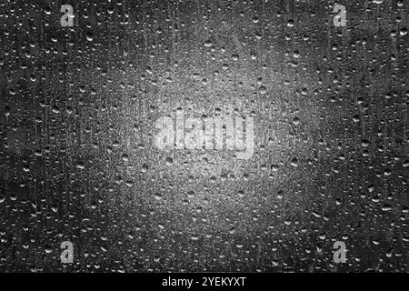 Gouttelettes d'eau sur la fenêtre en verre opaque en noir et blanc avec un phare brillant à travers Banque D'Images