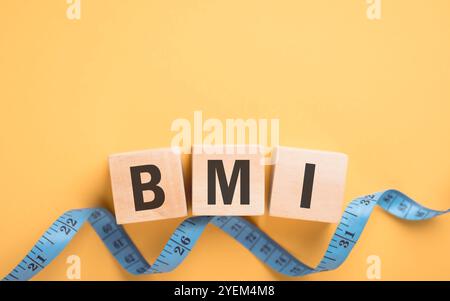 Bloc de bois de vue de dessus affichant 'IMC' à côté d'un ruban à mesurer sur fond jaune. Le concept d'indice de masse corporelle, soulignant l'importance de h. Banque D'Images