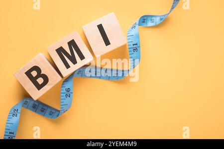 Bloc de bois de vue de dessus affichant 'IMC' à côté d'un ruban à mesurer sur fond jaune. Le concept d'indice de masse corporelle, soulignant l'importance de h. Banque D'Images