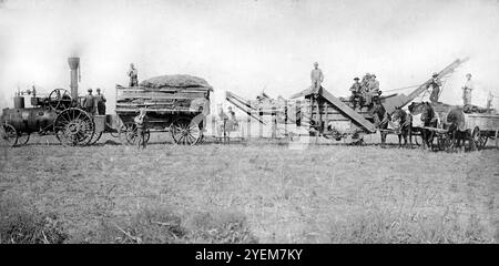 Les fermiers et leurs familles posent avec leur équipement de battage dans les grandes Plaines des États-Unis, vers 1900. Banque D'Images