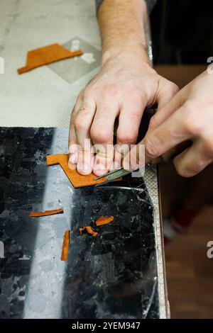 La main d'un homme tient des morceaux de cuir pour un portefeuille en cuir dans son atelier. Le processus de travail avec du cuir brun naturel. L'artisan tient le Banque D'Images