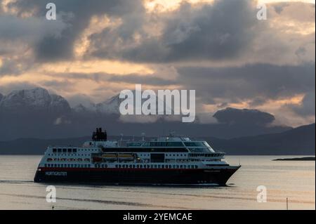 Le bateau de croisière Hurtigruten Trollfjord s'approche du terminal de croisière à Hastad alors que le soleil d'automne se lève sur la distance des montagnes enneigées et Banque D'Images