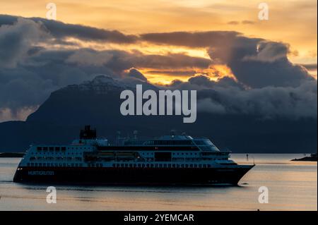 Le bateau de croisière Hurtigruten Trollfjord s'approche du terminal de croisière à Hastad alors que le soleil d'automne se lève sur la distance des montagnes enneigées et Banque D'Images