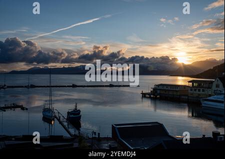 Lever le soleil d'automne sur les montagnes enneigées de loin et le Vagsfjorden avec un port et un port animés dans la petite ville de Harstad en Norvège, Banque D'Images