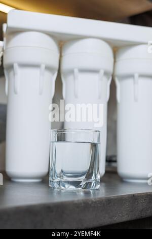 Un verre d'eau filtrée. Système de filtration d'eau avec cartouches remplaçables. Un système dans l'appartement avec trois réservoirs pour nettoyer l'eau du robinet. Banque D'Images