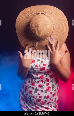 Belle femme debout portant une robe colorée avec un chapeau couvrant toute sa tête. Isolé sur fond fumé coloré. Banque D'Images