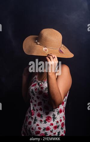 Belle femme debout portant une robe colorée avec un chapeau couvrant toute sa tête. Isolé sur fond fumé coloré. Banque D'Images