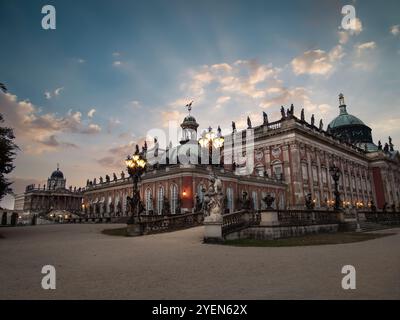 Vue en soirée sur le château de Sanssouci et le nouveau palais de Potsdam, en Allemagne, avec une architecture baroque illuminée par un éclairage tamisé et un ciel crépusculaire serein Banque D'Images