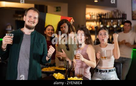 Filles heureuses adm hommes avec drapeau belge célèbre la victoire de son équipe préférée dans le bar à bière Banque D'Images