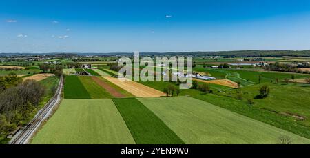 Une vue panoramique révèle de vastes champs patchwork de vert et d'or éclatants, sur un ciel bleu clair. Une ligne de chemin de fer longe un bord, Highli Banque D'Images