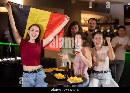 Filles heureuses adm hommes avec drapeau belge célèbre la victoire de son équipe préférée dans le bar à bière Banque D'Images