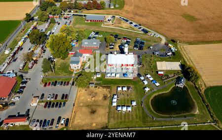 Une perspective aérienne met en valeur une zone d'événements communautaires animée avec des tentes et divers véhicules stationnés à proximité, entourés de terres agricoles luxuriantes, Highlighti Banque D'Images