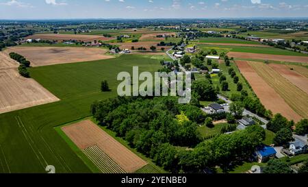 Une vue aérienne panoramique capture un paysage rural dynamique avec des champs verts, des parcelles de terres agricoles brunes et une petite communauté nichée au milieu de la verdure par une journée ensoleillée. Banque D'Images