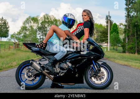 Un couple multiracial pose avec amour à côté de leur moto dans un champ verdoyant et luxuriant. Embrassés, ils sourient avec fierté, capturant à la fois leur lien profond A. Banque D'Images