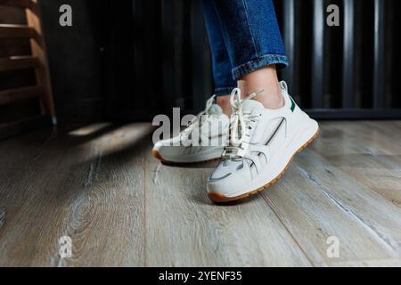 Jambes féminines élancées gros plan en Jean et baskets blanches en cuir véritable. Banque D'Images