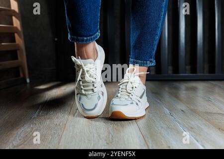 Jambes féminines élancées gros plan en Jean et baskets blanches en cuir véritable. Banque D'Images