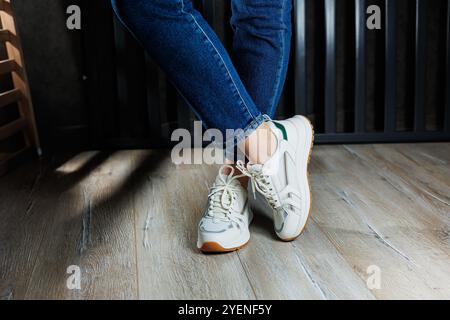 Jambes féminines élancées gros plan en Jean et baskets blanches en cuir véritable. Banque D'Images