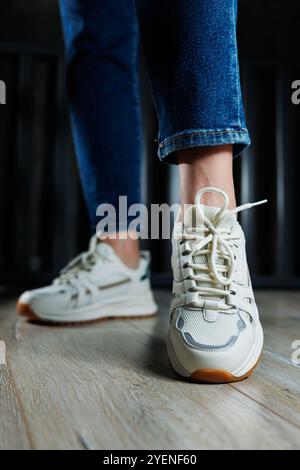 Jambes féminines élancées gros plan en Jean et baskets blanches en cuir véritable. Banque D'Images