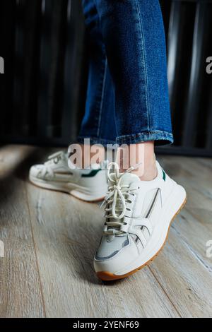 Jambes féminines élancées gros plan en Jean et baskets blanches en cuir véritable. Banque D'Images