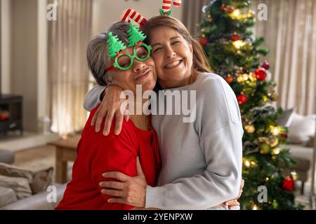 Amies féminines seniors serrées joyeusement près de l'arbre de Noël, célébrant les vacances ensemble, à la maison. Personnes âgées, bonheur, amitié, célébration, festive, Banque D'Images