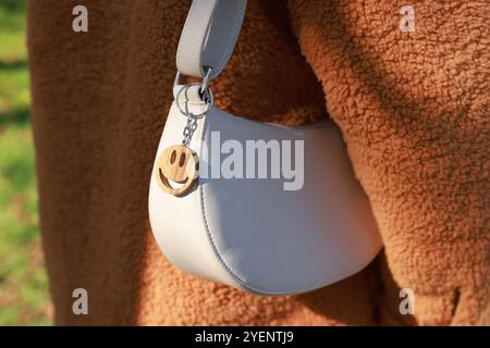 Femme avec porte-clés en bois en forme de visage souriant sur son sac à l'extérieur, gros plan. Mise au point sélective Banque D'Images