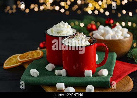 Savoureuses boissons chaudes au cacao avec de la crème fouettée dans des tasses et des guimauves sur une table noire, gros plan Banque D'Images