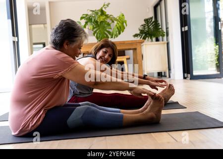 Amies féminines seniors s'étirant sur des tapis de yoga à la maison, profitant de l'exercice ensemble. Fitness, bien-être, mode de vie sain, activité de groupe, entraînement à domicile Banque D'Images