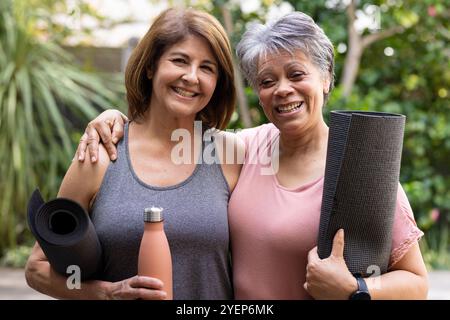 Tenant des tapis de yoga et une bouteille d'eau, amies féminines seniors souriant à l'extérieur dans l'amitié. Bien-être, fitness, mature, exercice, santé, actif Banque D'Images