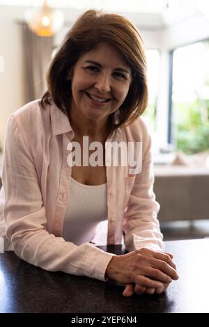 Femme senior souriante appuyée sur le comptoir de cuisine à la maison, profitant du moment. Personnes âgées, bonheur, style de vie, relaxation, femme âgée Banque D'Images