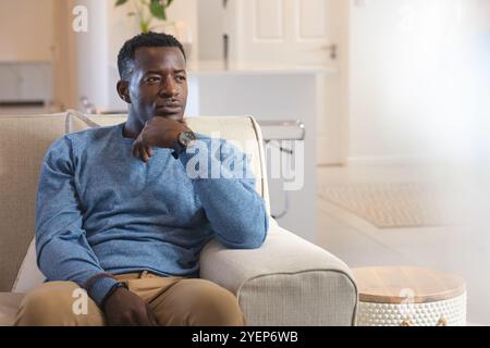 Réfléchi afro-américain homme afro-américain se relaxant sur le canapé à la maison, portant un pull bleu. Détente, tranquillité, confortable, à l'intérieur, style de vie, le Banque D'Images