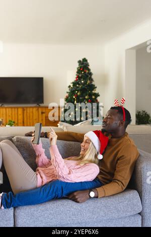 Couple multiracial se relaxant sur le canapé, profiter de l'appel vidéo de vacances par arbre de Noël, à la maison. célébration, connexion, festif, famille, communication, Banque D'Images