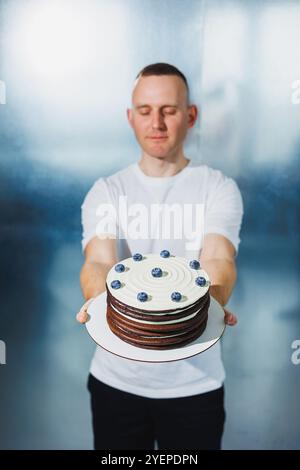 Un jeune confiseur tient un gâteau aux fruits sucrés frais dans ses mains. Un homme présente un gâteau. Banque D'Images