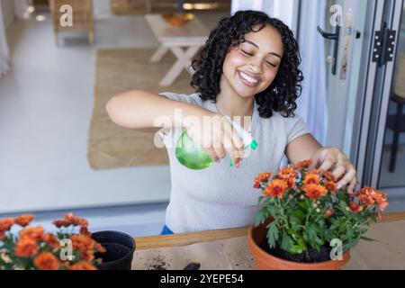 Femme souriante arrosant des fleurs en pot à la maison, profitant du jardinage à l'intérieur. plantes, horticulture, bonheur, plantes d'intérieur, culture, style de vie Banque D'Images