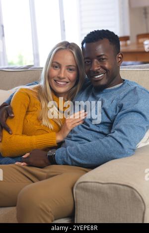 Couple multiracial souriant se relaxant sur un canapé confortable à la maison pendant Noël. Célébration, vacances, festif, multiculturel, détente, hiver Banque D'Images