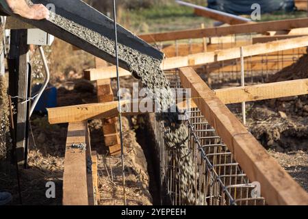 Un travailleur de la construction verse du béton d'un malaxeur de béton dans les fondations d'une maison sur un chantier de construction Banque D'Images