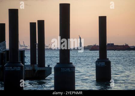 Photographie capturant la Statue de la liberté au coucher du soleil, encadrée par plusieurs piliers de quai au premier plan. Banque D'Images