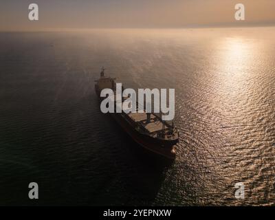 Drone aérien vidéo d'un cargo naviguant sur des eaux brumeuses avec des reflets de soleil, créant une scène maritime calme et mystérieuse, parfaite pour Banque D'Images