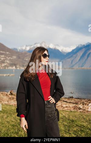 Belle jeune femme en manteau noir, chemisier rouge et lunettes de soleil Banque D'Images