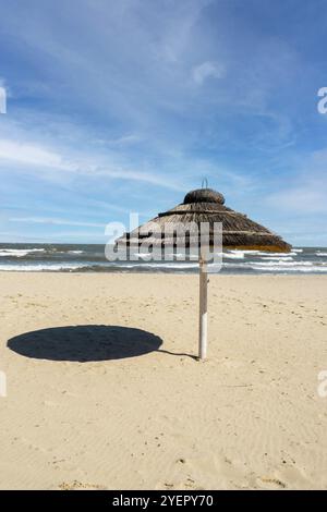 Parasol en rotin de plage de paille à la plage vide avec des fonds de ciel bleu mer côte océan. Journée de détente. Copiez l'espace pour votre texte. Voyage idyllique et su Banque D'Images