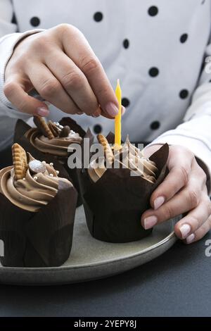 Les mains des femmes font de délicieux petits gâteaux au chocolat avec de la crème sur fond sombre. Trois muffins au chocolat. Gâteau d'anniversaire préparation de fête. Choco. Maison Banque D'Images