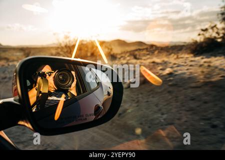 Photographe dans un rétroviseur de voiture capturant une scène de coucher de soleil dans le désert Banque D'Images