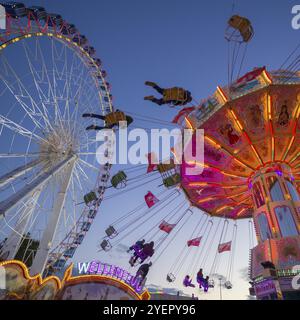 Une foire au crépuscule avec carrousel à chaînes illuminées et grande roue, Europa Rad, manèges, vol des vagues, Cannstatter Wasen, Festival folklorique, Bad Cannstatt, S. Banque D'Images