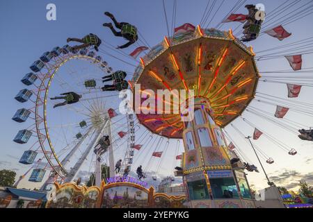 Une foire au crépuscule avec carrousel à chaînes illuminées et grande roue, Europa Rad, manèges, vol des vagues, Cannstatter Wasen, Festival folklorique, Bad Cannstatt, S. Banque D'Images