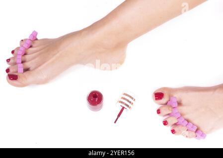 Application de pédicure sur les pieds de la femme avec des ongles rouges, dans des séparateurs d'orteils roses, sur fond blanc isolé Banque D'Images