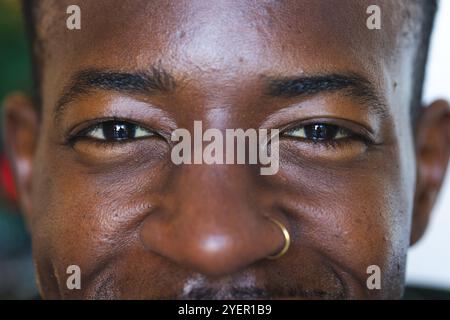 Homme afro-américain souriant avec anneau de nez profitant de l'atmosphère festive de vacances à la maison. Célébration, bonheur, joyeux, décoration, confortable, saisonnier Banque D'Images