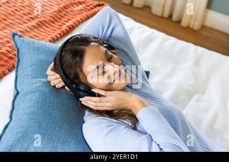 Détente à la maison, femme profitant de la musique avec des écouteurs, souriant paisiblement. Loisirs, détente, écoute de musique, cosy, tranquillité, style de vie Banque D'Images