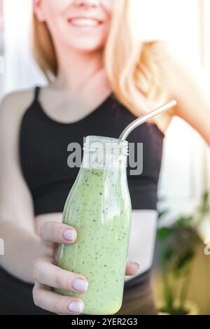 Jeune femme blonde millénelle boit du smoothie végétalien Detox. Femme faisant des exercices de yoga à la maison. Alimentation propre, perte de poids, alimentation saine c Banque D'Images